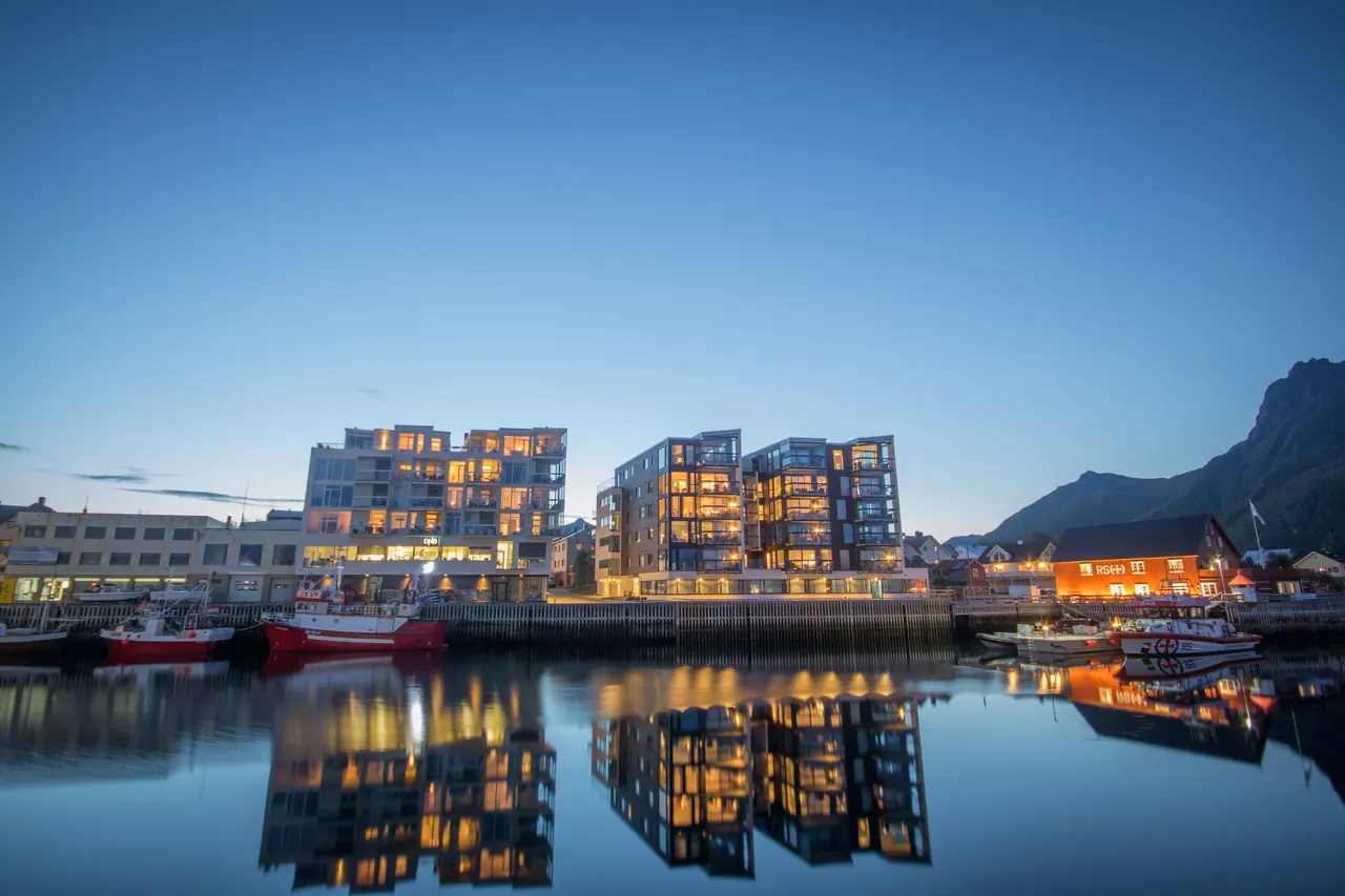 Modern buildings illuminated at dusk with reflections on calm waterfront, showcasing Scandinavian architecture.