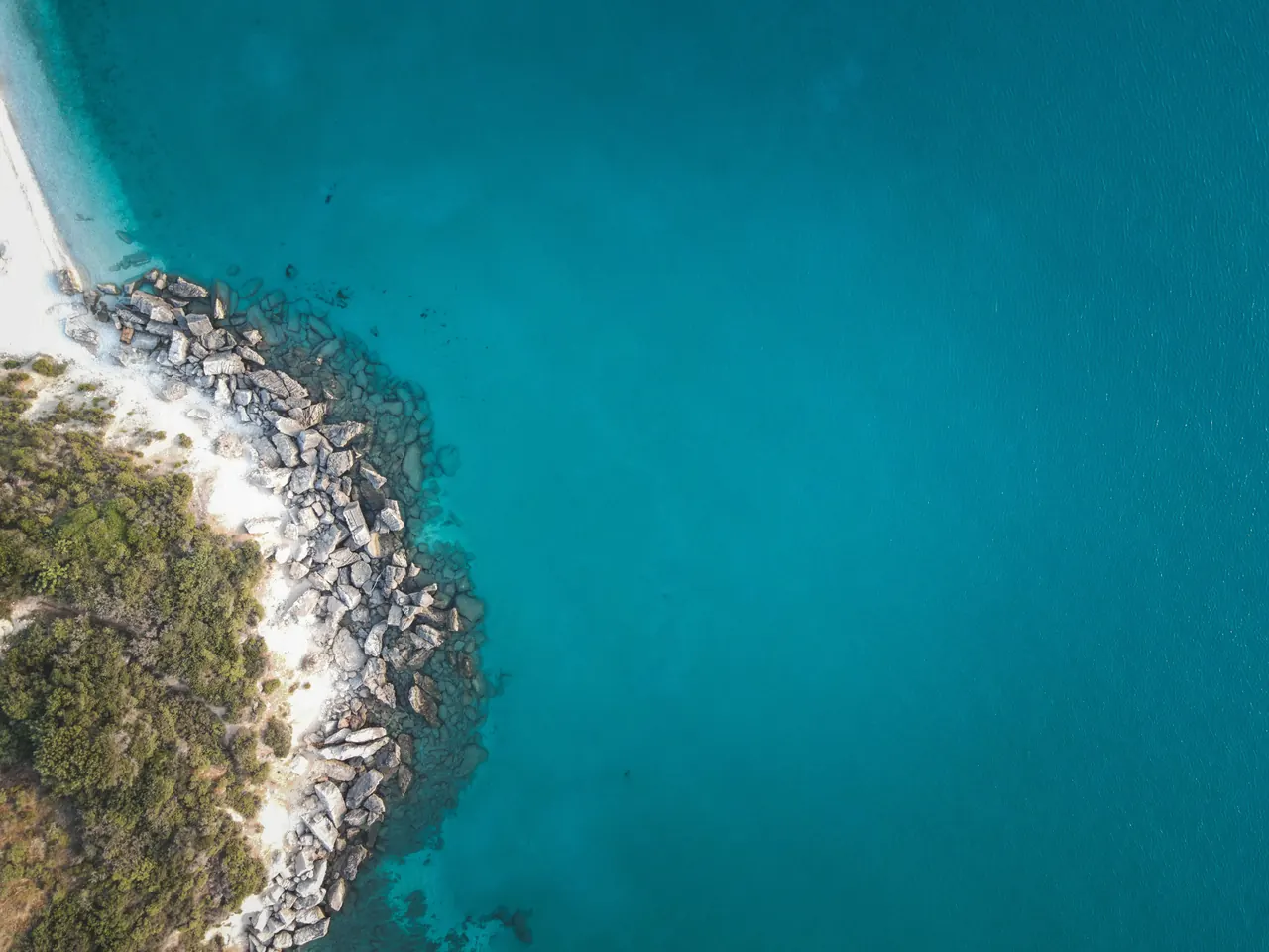 Stunning aerial shot of a rocky coastline meeting clear turquoise waters, showcasing natural beauty.