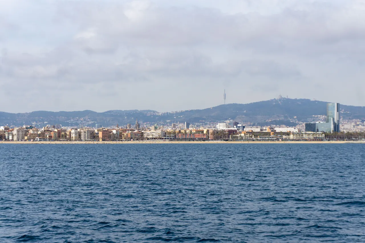Stunning panoramic view of Barcelona coastline with urban skyline and distant hills under a cloudy sky.