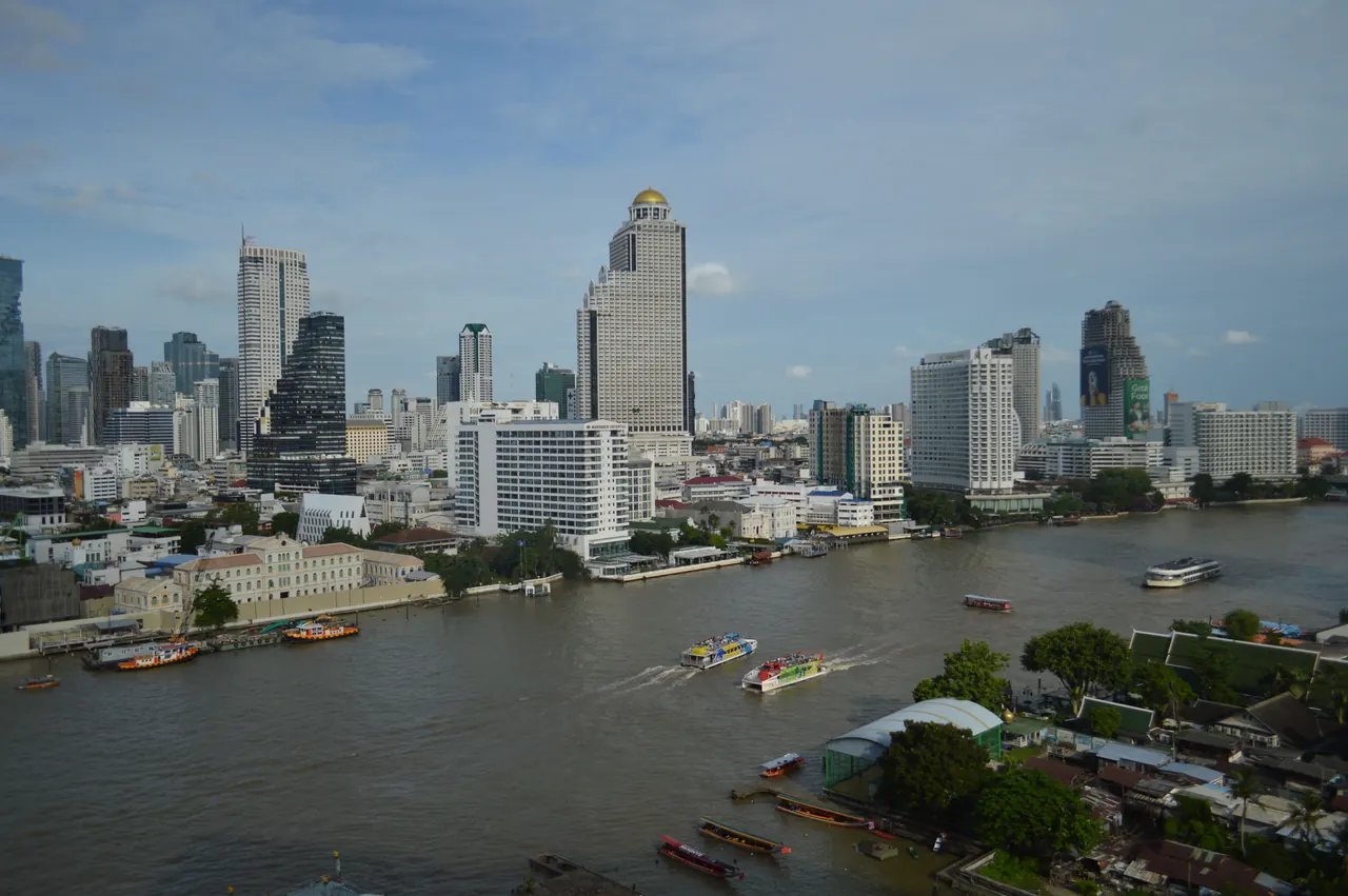 A scenic view of Bangkok’s skyline along the Chao Phraya River with boats navigating the water.