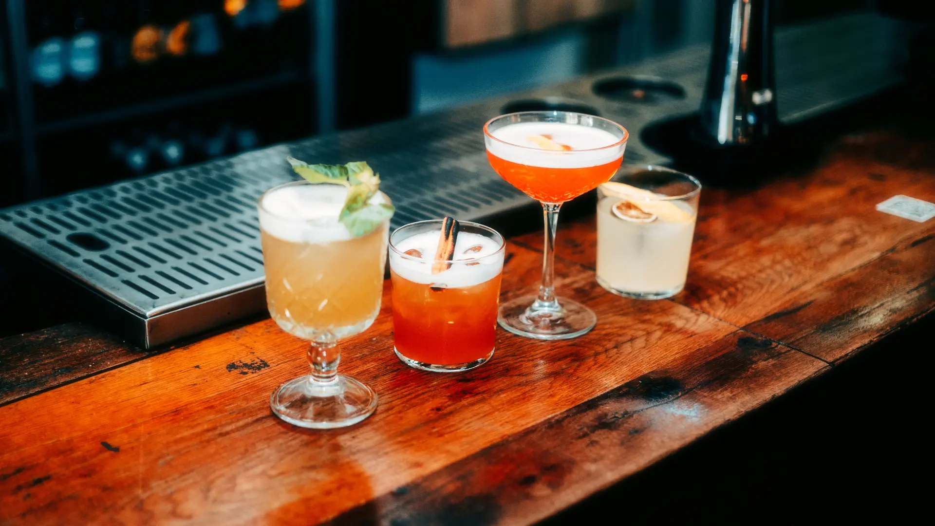 A row of colourful cocktails lined up along a wooden bar