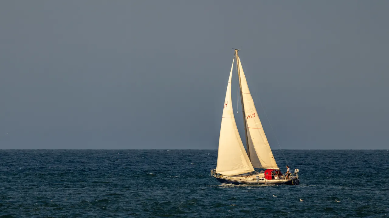 A tranquil sailboat glides on the open sea under a sunset sky, creating a peaceful maritime scene.