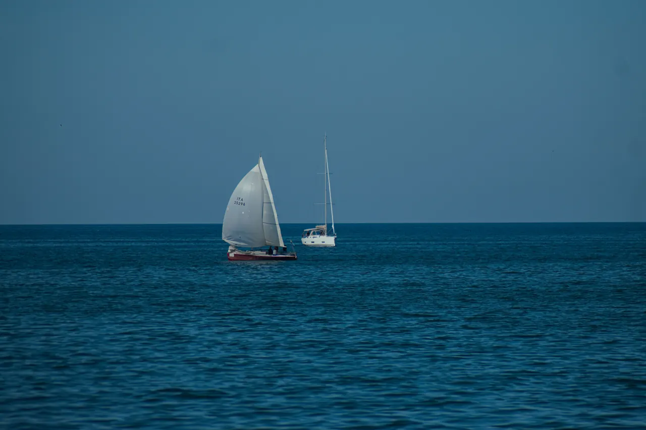 Two sailboats glide across a serene blue sea under a clear sky, showcasing peaceful maritime travel.