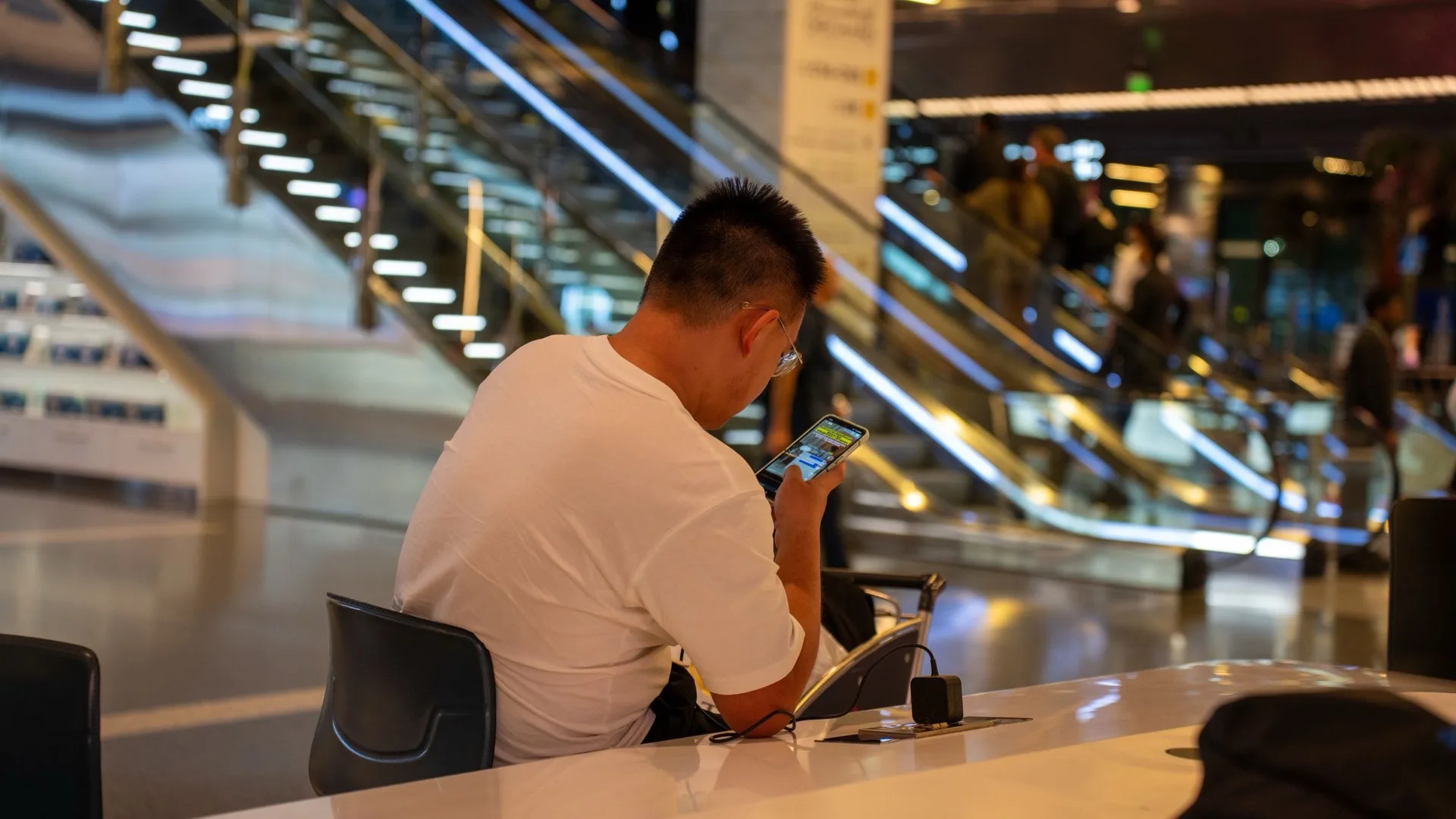 A traveler working on a phone at a counter in a modern airport terminal