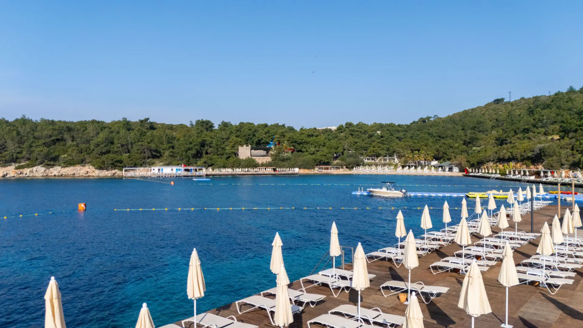 A calm lagoon beach lined with loungers and umbrellas under a bright blue sky