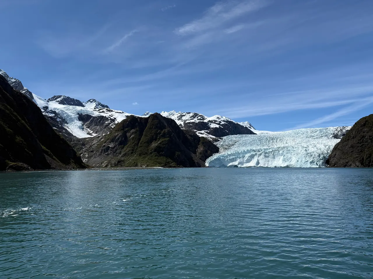 A glacier meeting icy green water between steep mountains in Kenai Fjords National Park, Alaska