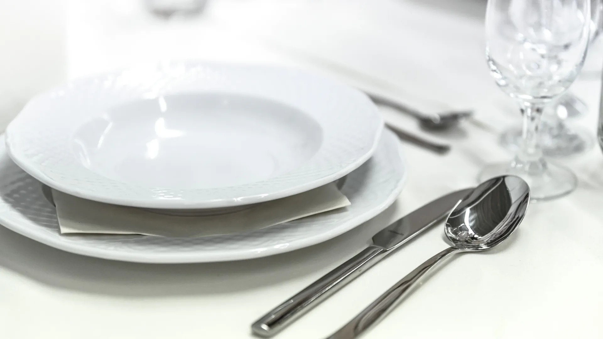 A laid restaurant table with white porcelain, cutlery and a wine glass