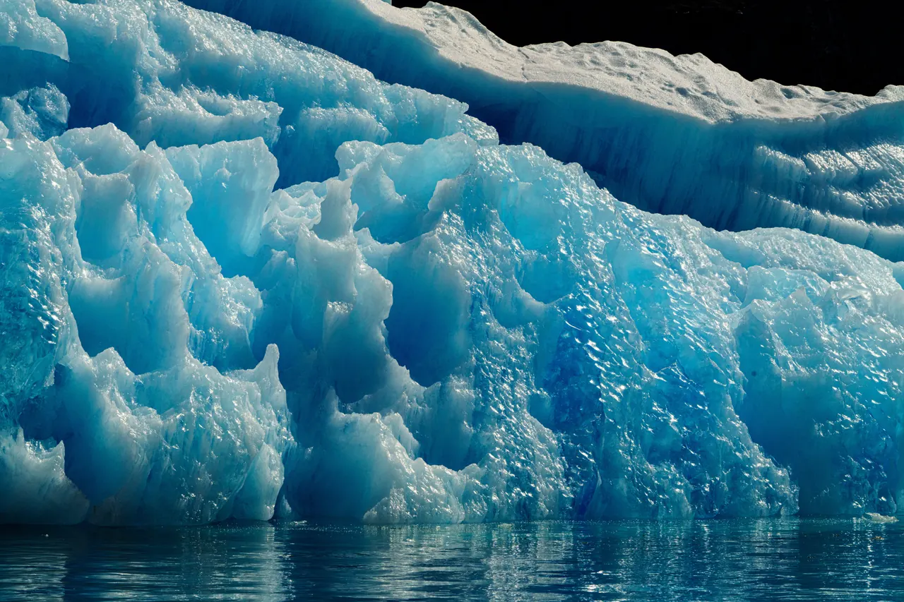 A stunning view of a blue iceberg with intricate textures, floating in the calm ocean.