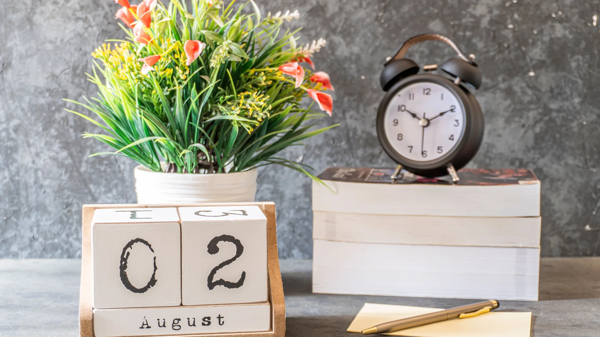 A desk calendar and a small clock beside a notepad