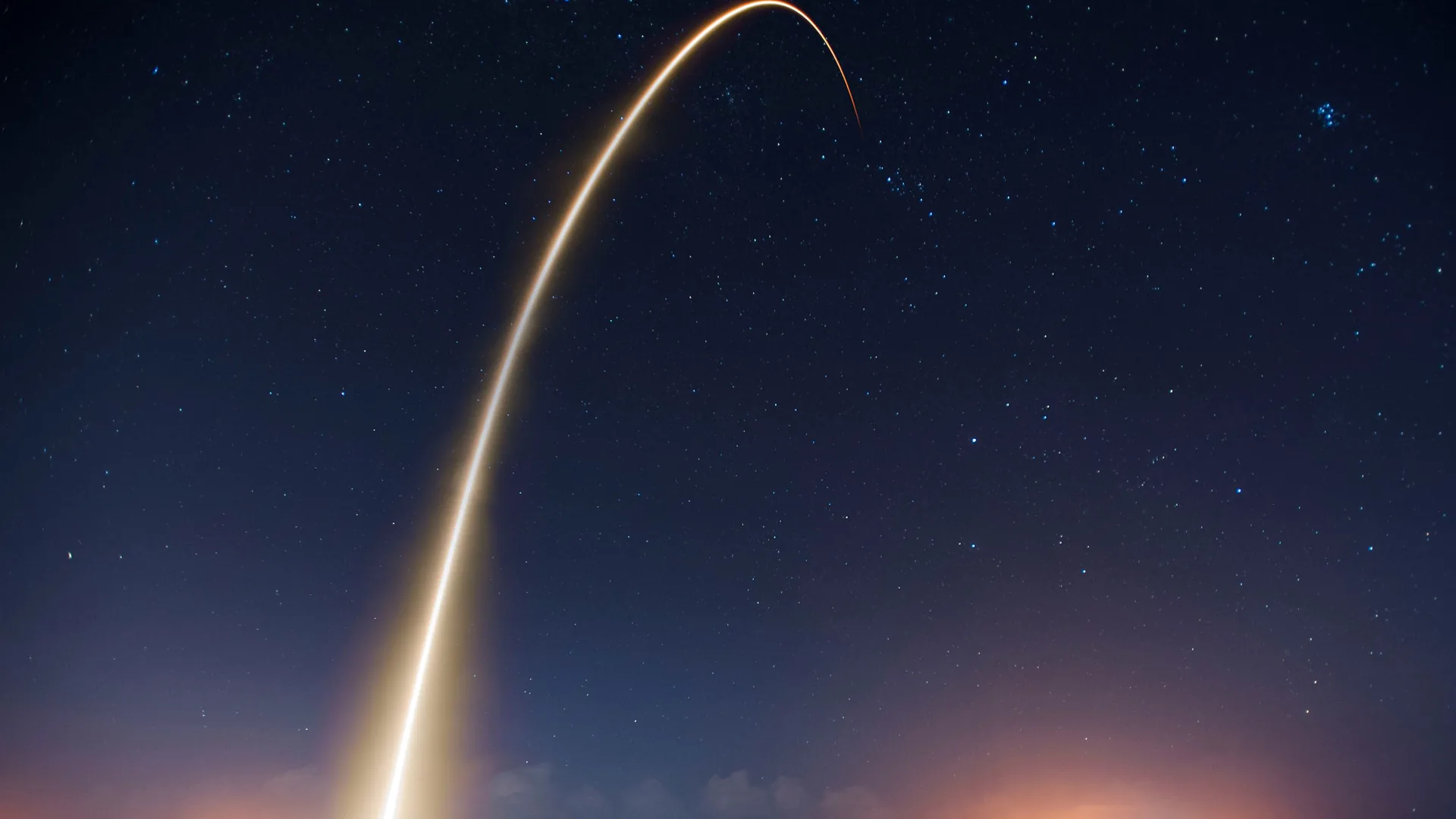 A long-exposure photograph of a rocket launch arcing across a star-filled night sky