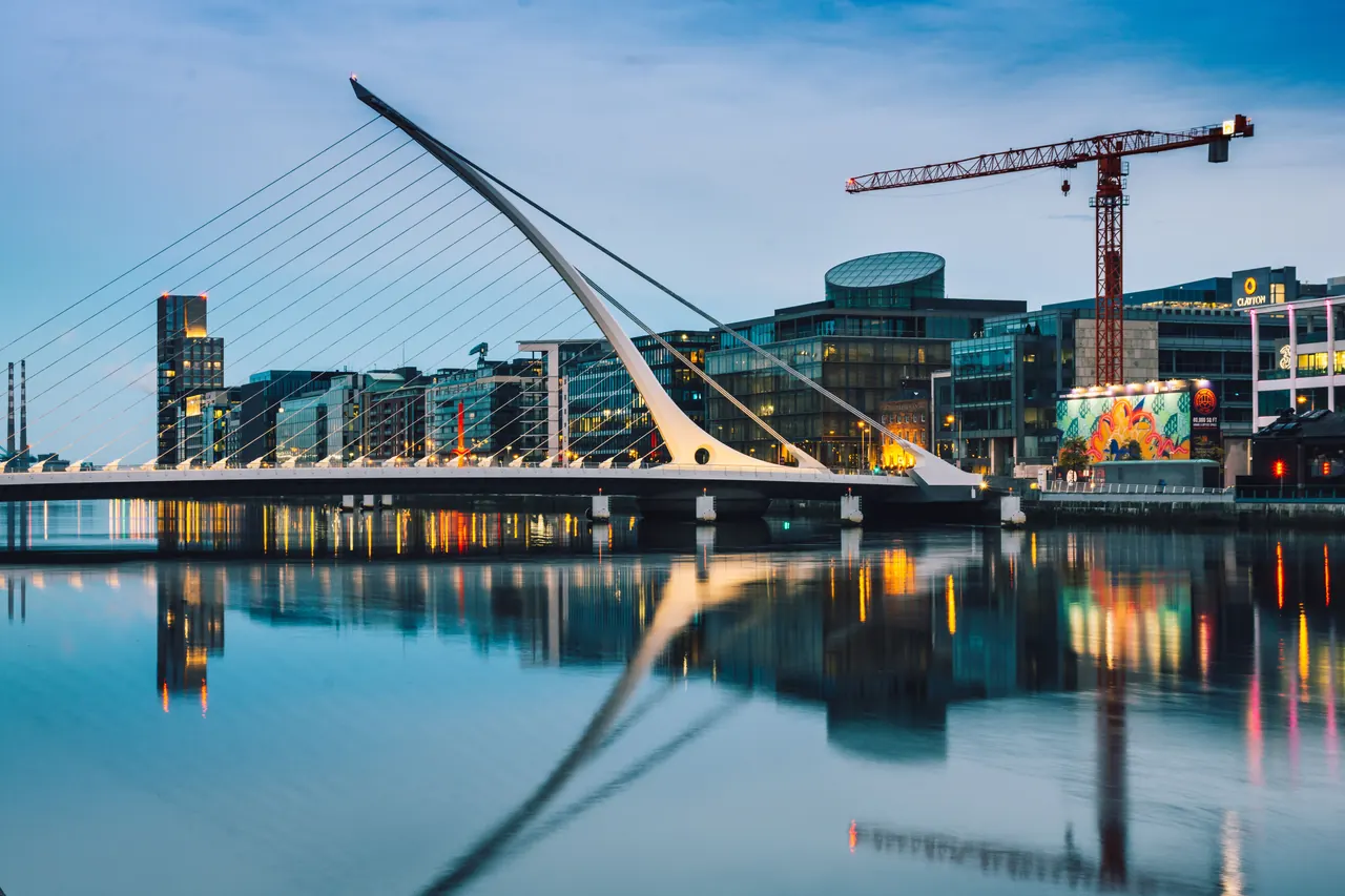The Samuel Beckett Bridge lit at twilight, its harp-shaped cables reflected in the River Liffey