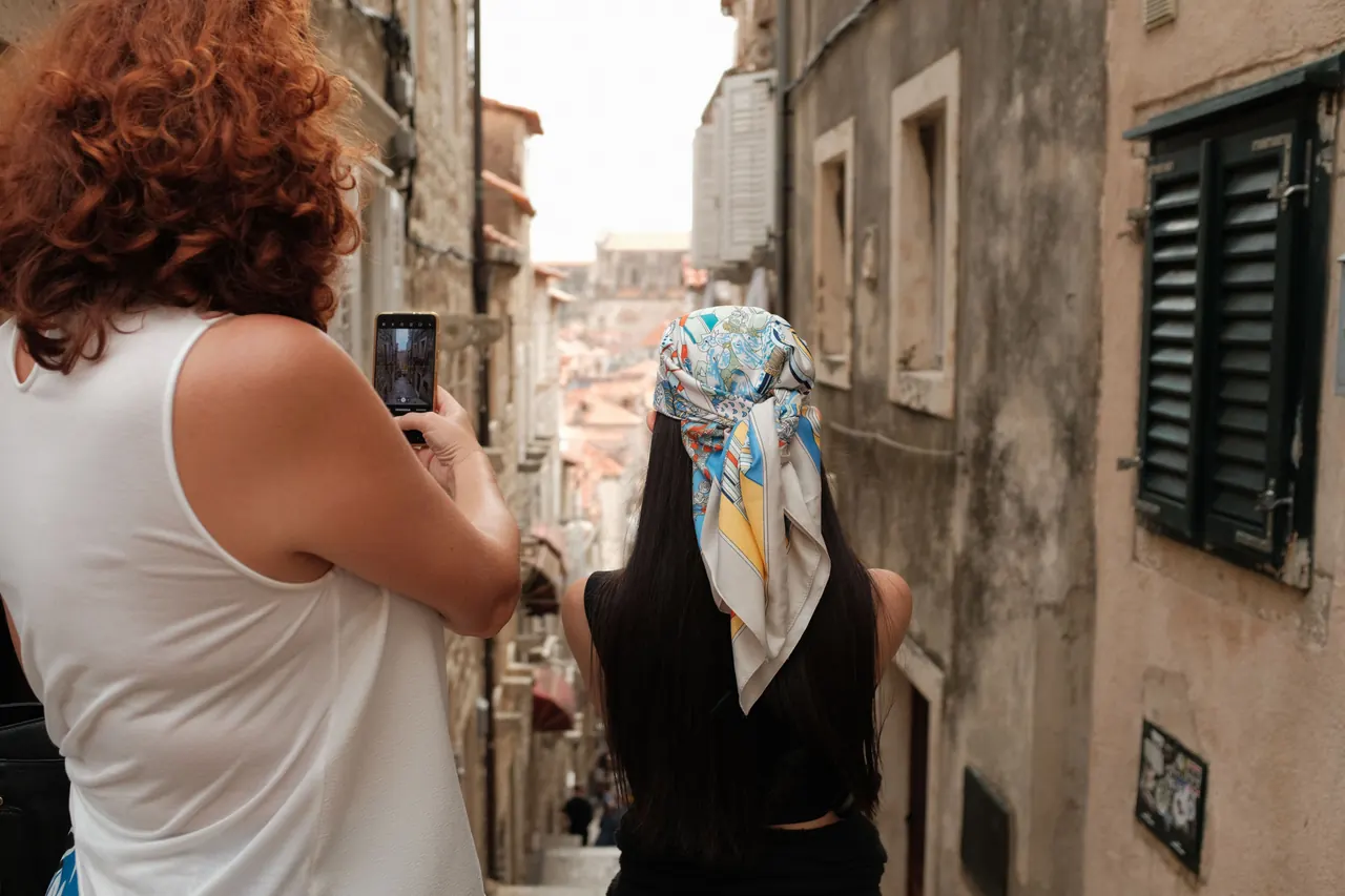A narrow stepped alley climbing between stone buildings in Dubrovnik's Old Town, with two people walking up it