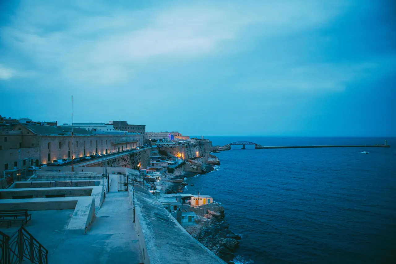 A serene coastal cityscape captured at dusk showing a seaside view with a unique architectural shoreline.
