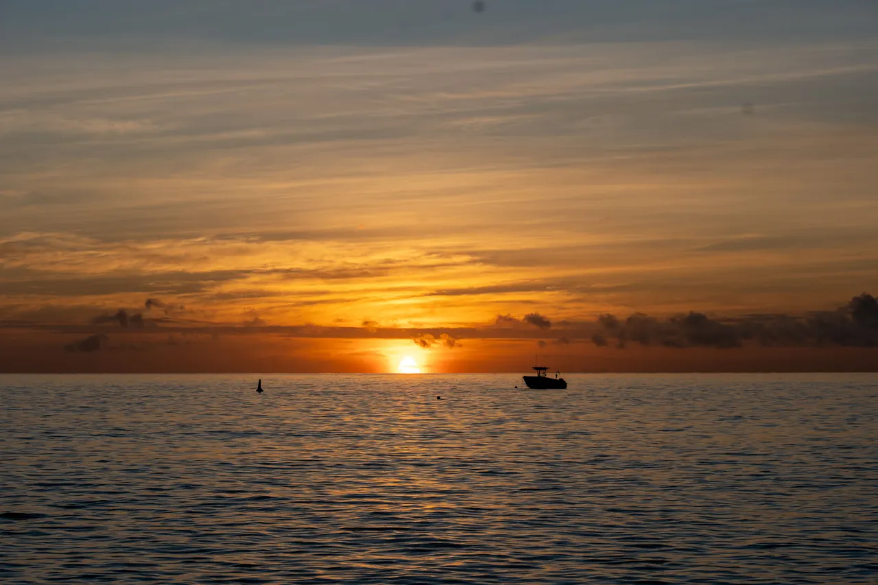 A tranquil sunset over the ocean with a silhouette of a boat, offering a stunning view.