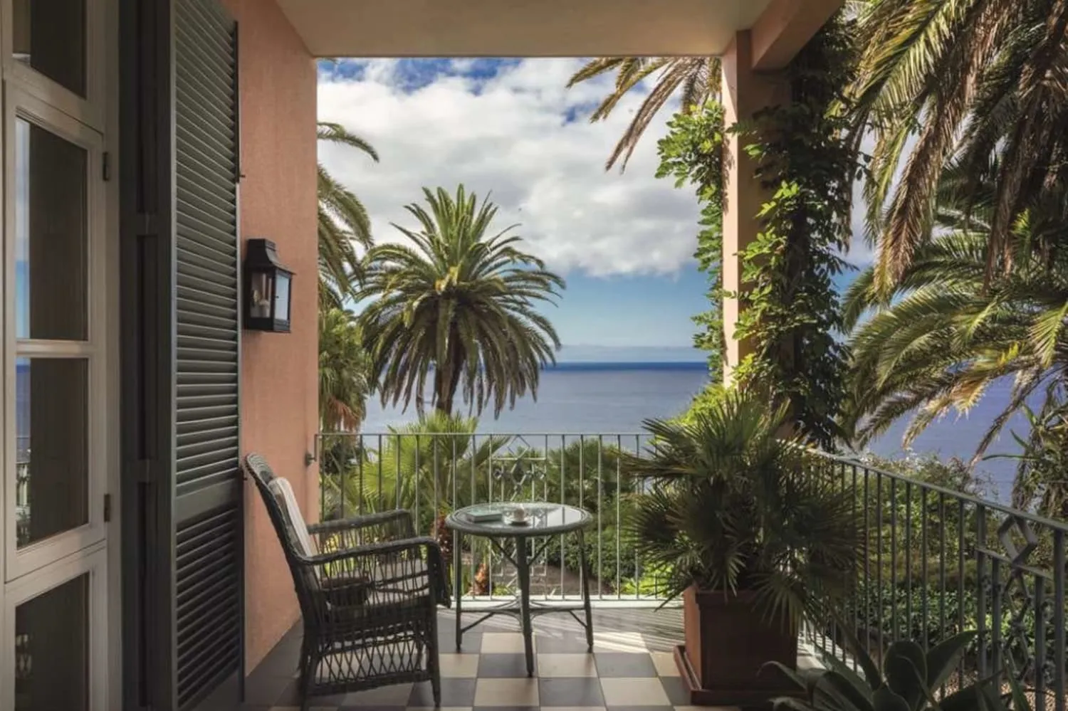 A pink-walled balcony framed by palm trees, looking out over the Atlantic at Reid's Palace, Madeira