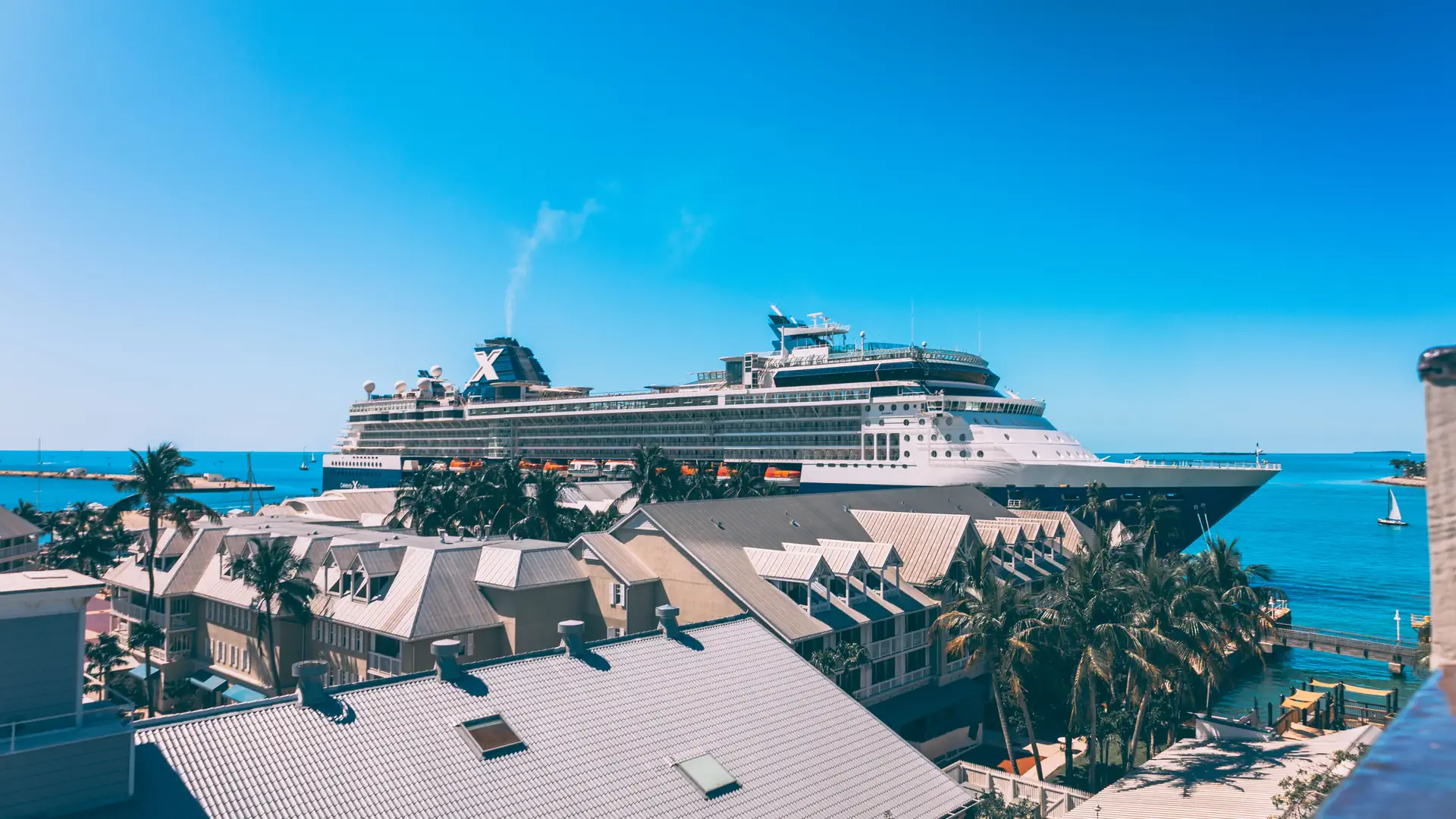 A large white cruise ship docked at a sunny waterfront pier under a clear blue sky