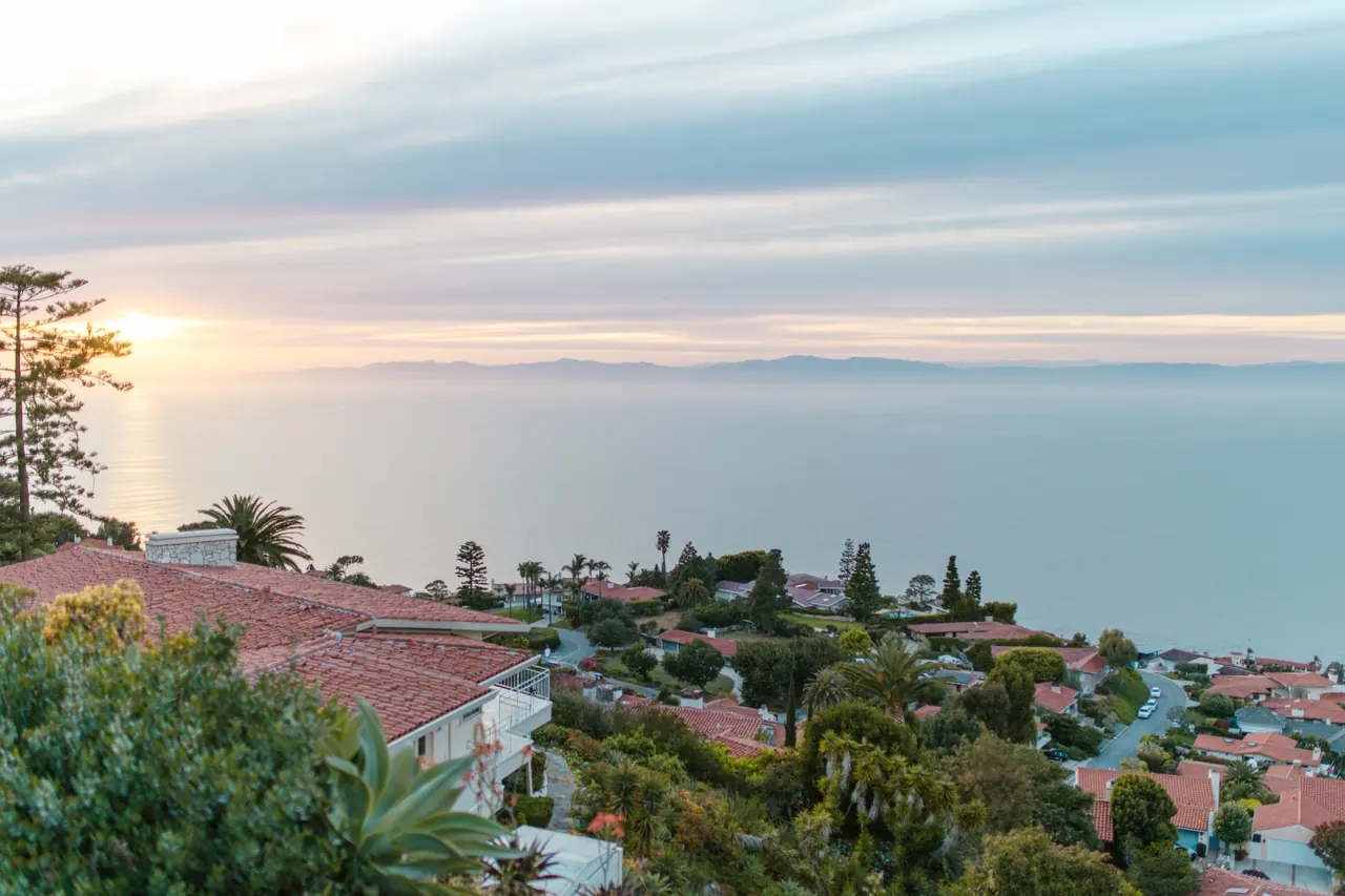 Serene view of a coastal town with red rooftops overlooking the ocean at sunrise, offering a tranquil ambiance.