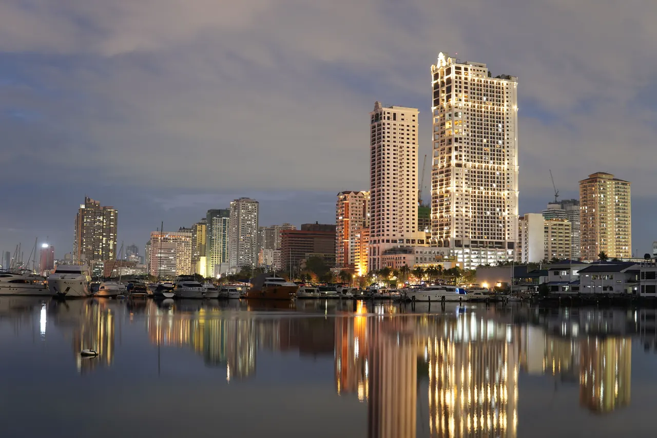 Stunning twilight view of Manila’s skyline reflecting on a calm body of water, featuring tall buildings and a serene atmosphere.