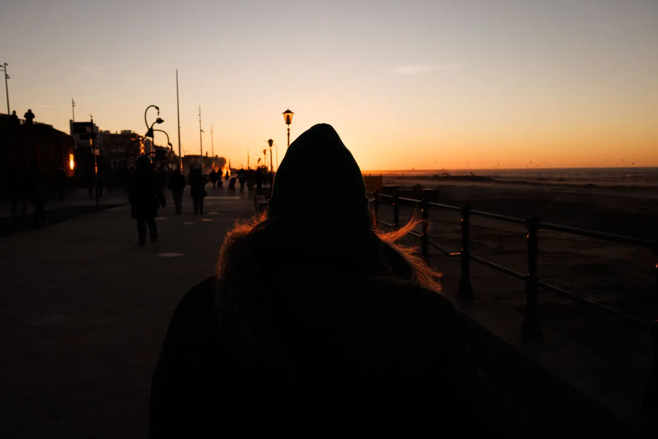 People walking along a promenade at sunset, silhouetted against the sky. Urban and serene.