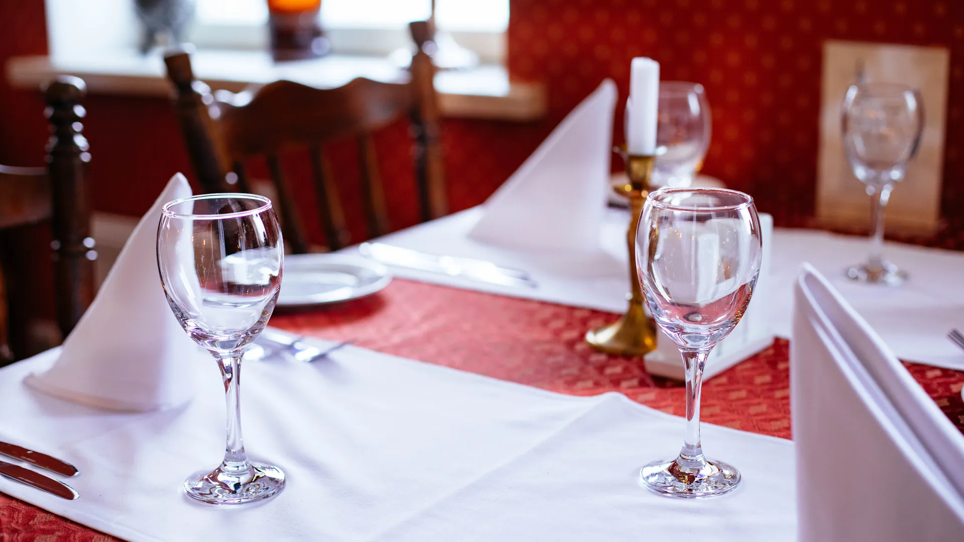 A restaurant table set with wine glasses, napkins and candles