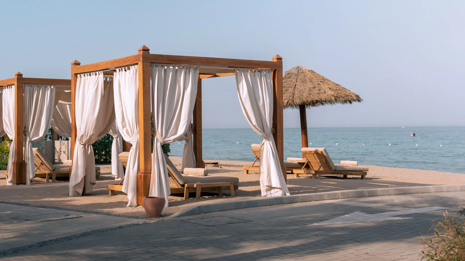 Timber beach cabanas with white curtains facing a calm turquoise sea
