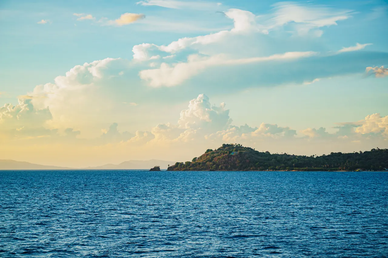 Serene view of an island’s green coastline under a vibrant sunset sky, with calm blue ocean waves.