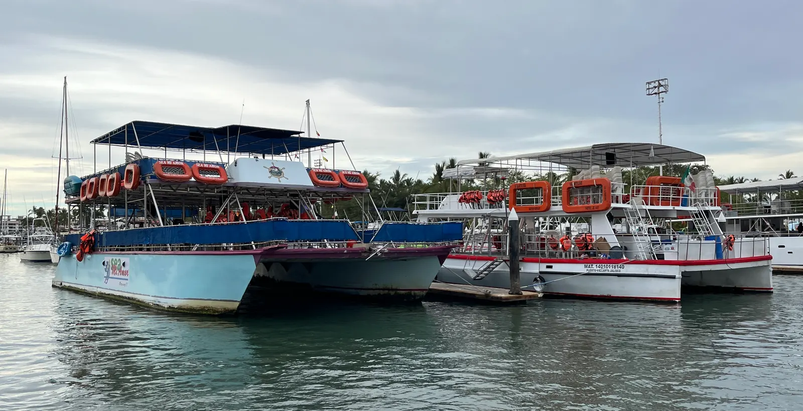 Open-air tour catamarans moored at Puerto Vallarta under a soft gray sky, life rings along their rails
