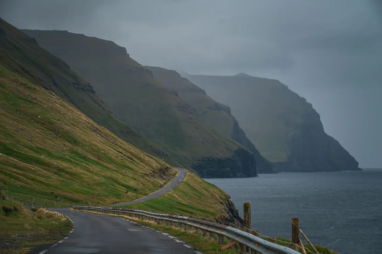 Stunning view of a winding road by dramatic cliffs and ocean under a cloudy sky.
