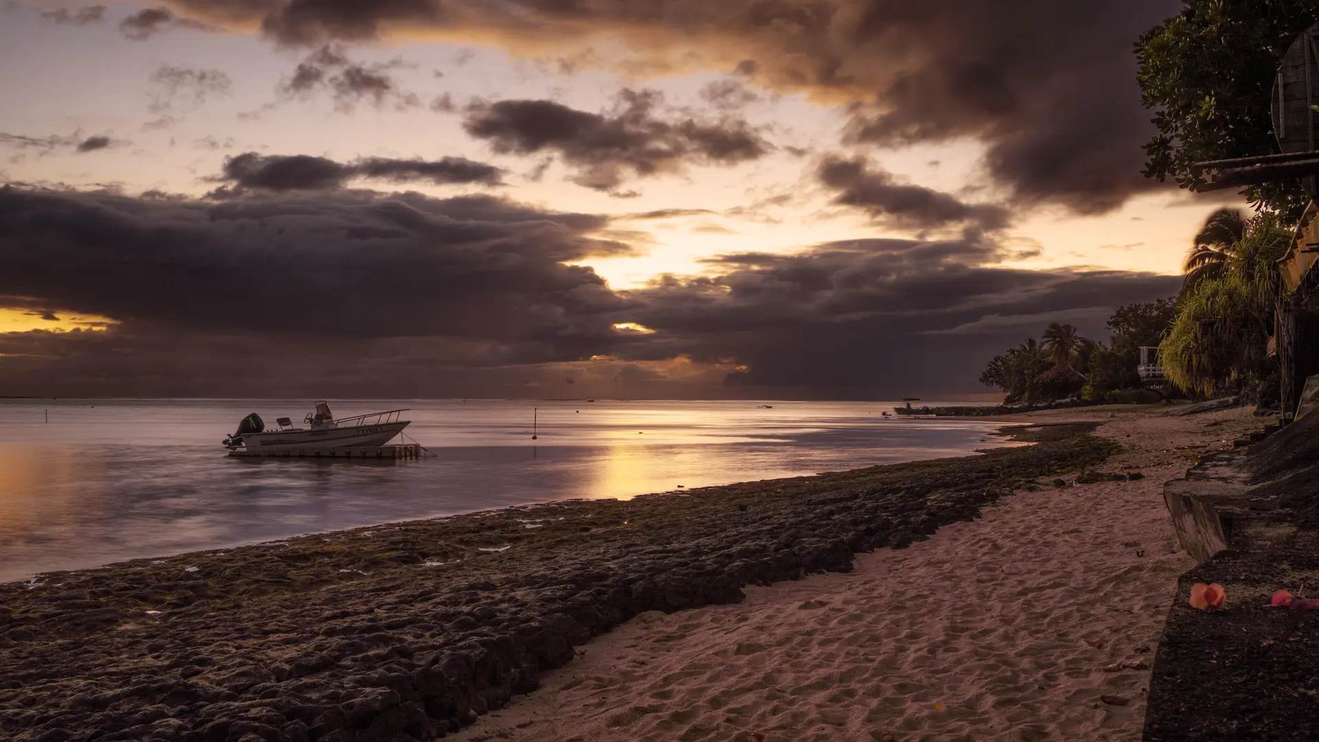 A small boat resting on calm water at sunset off a Moorea beach under dramatic clouds