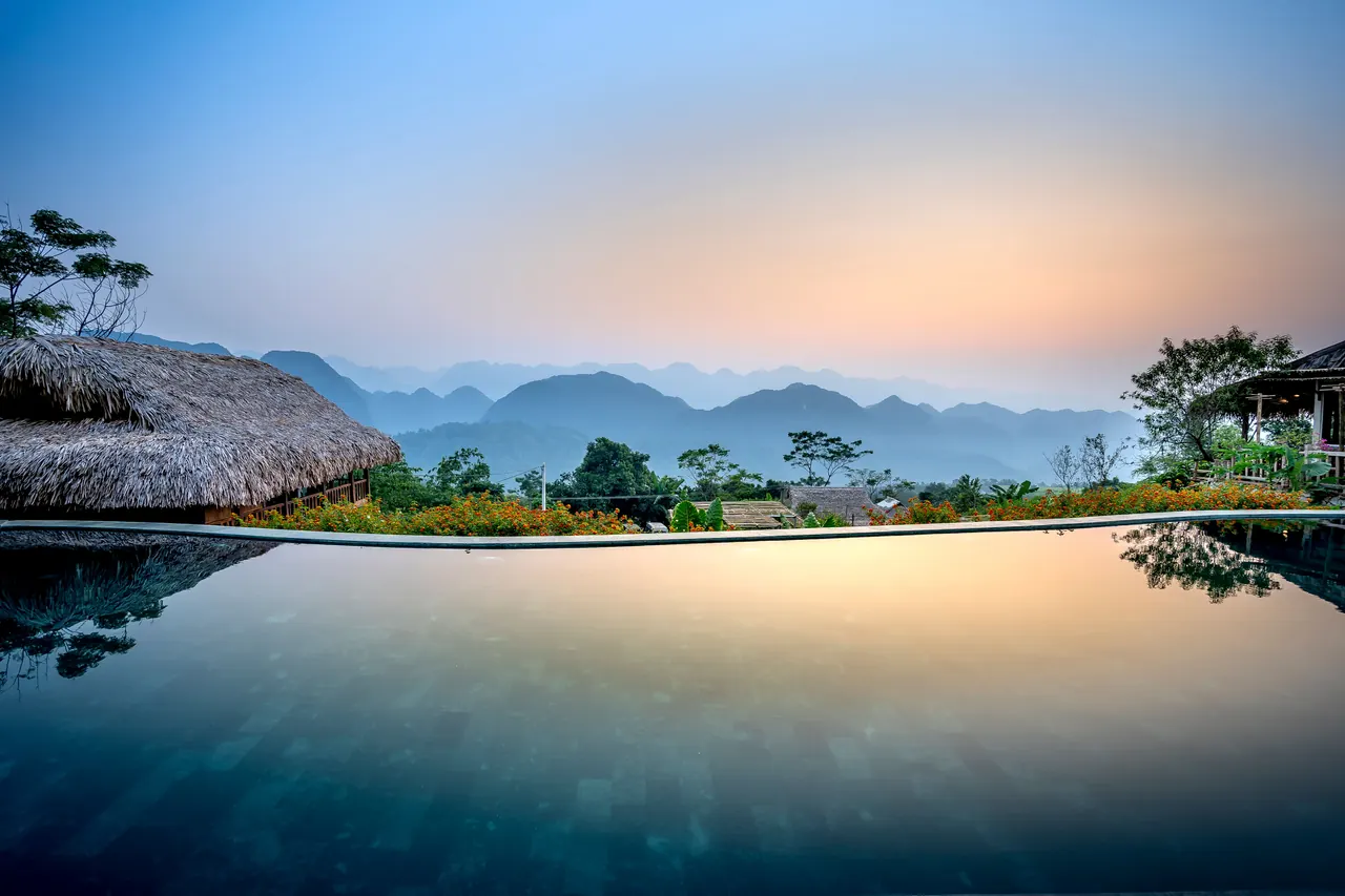 Clean water of pool located on tropical resort with wooden bungalows against silhouettes of mountain ridge on evening time in nature