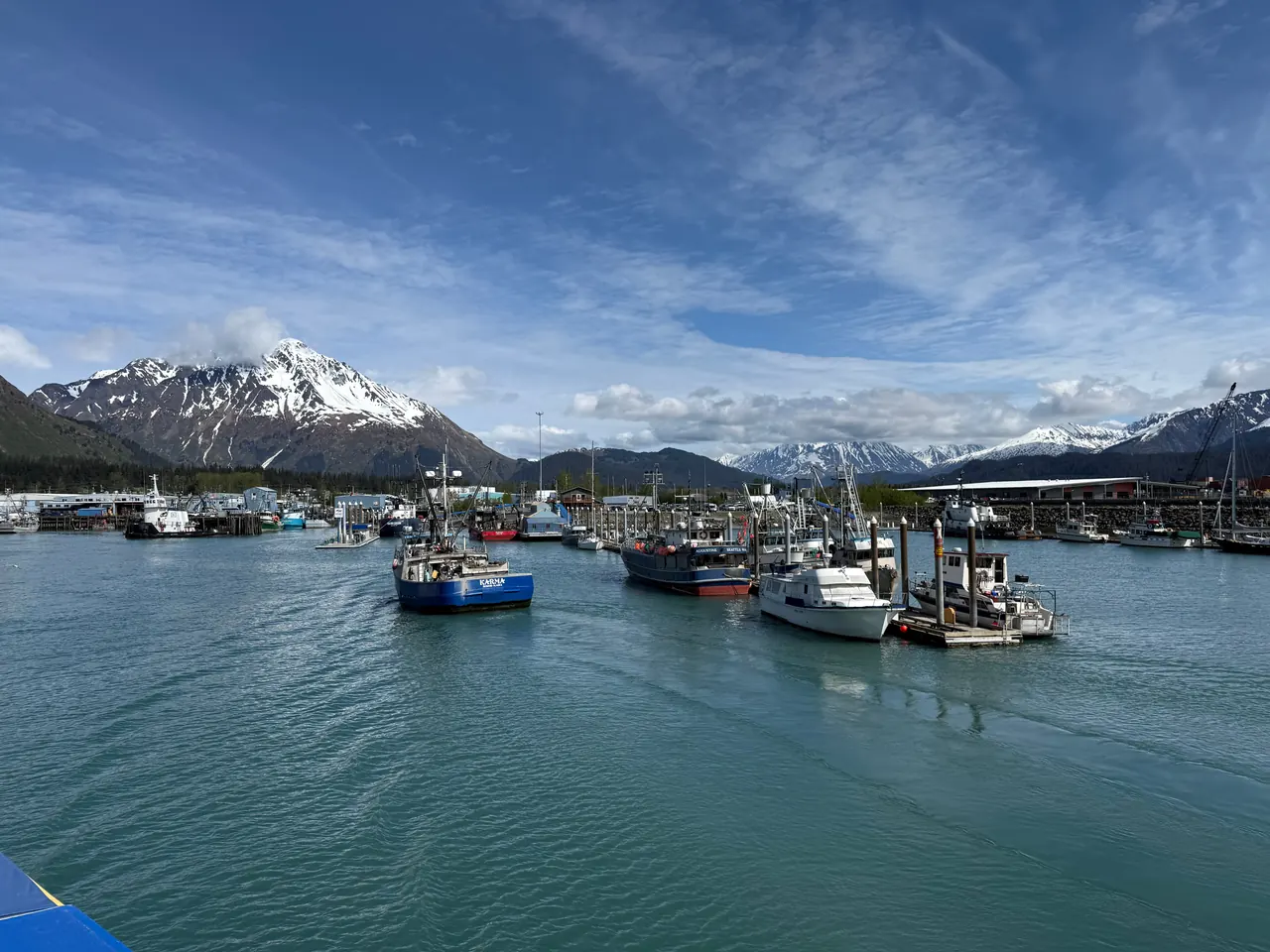 Boats docked at Seward harbor with scenic mountains and a clear blue sky in the background.