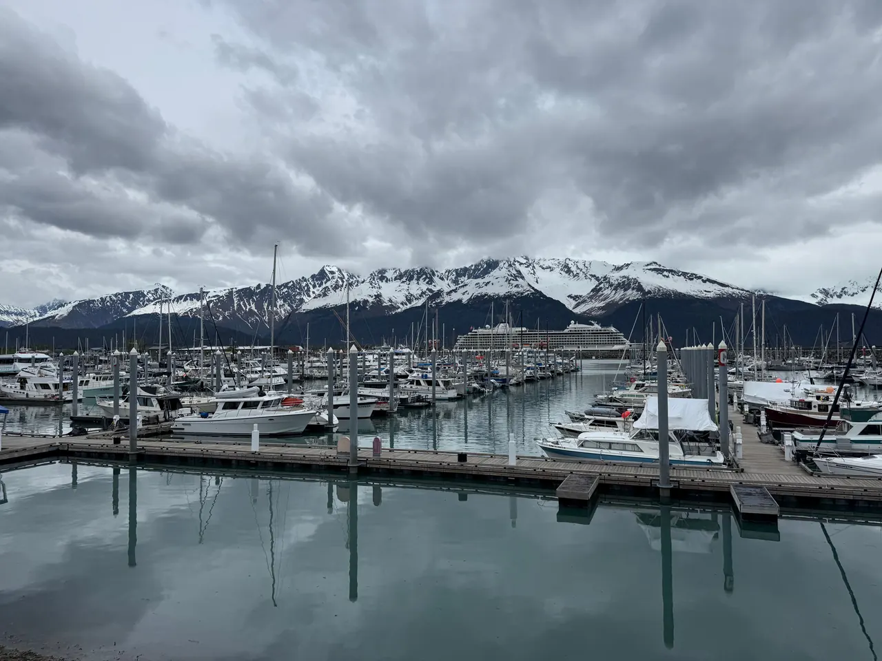 Scenic view of Seward Harbor with boats and snow-capped mountains under a cloudy sky.