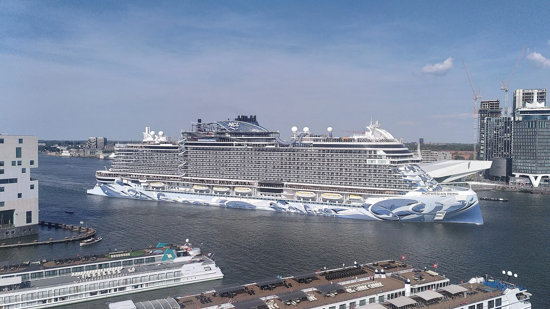 Norwegian Prima under way in Amsterdam, seen from above with river cruisers in the foreground