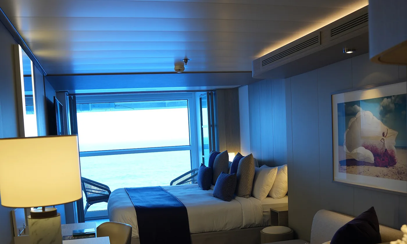 An Infinite Veranda stateroom aboard Celebrity Apex, with the balcony glass retracted to open the room to the sea