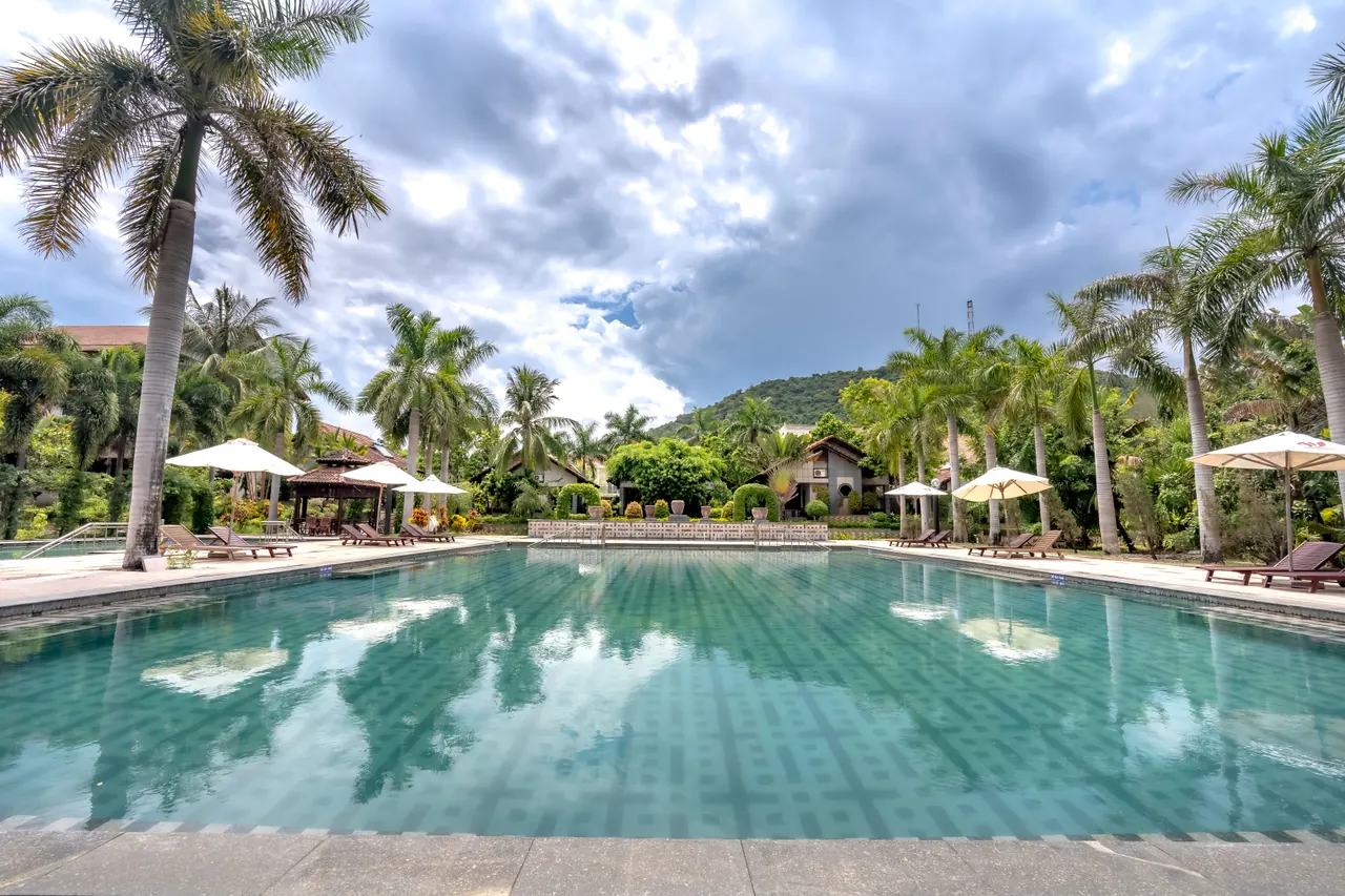 A tranquil tropical resort featuring a stunning pool surrounded by palm trees under a dramatic sky.