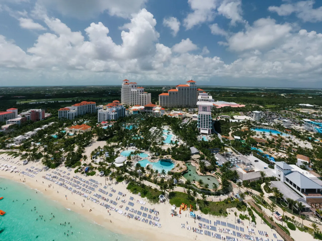 Aerial view of a Bahamian beach resort with pools, palm trees and pale sand beside clear water