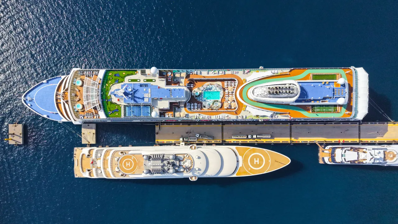Aerial view of two large cruise ships moored alongside each other at a sunlit port, their top-deck pools visible