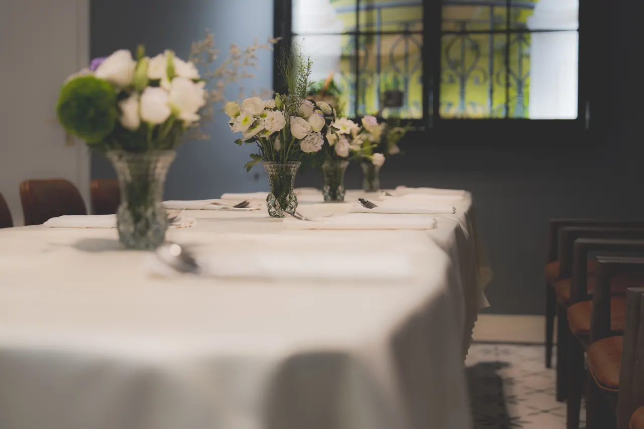 A formally laid restaurant table with white linen, glassware and a floral centerpiece