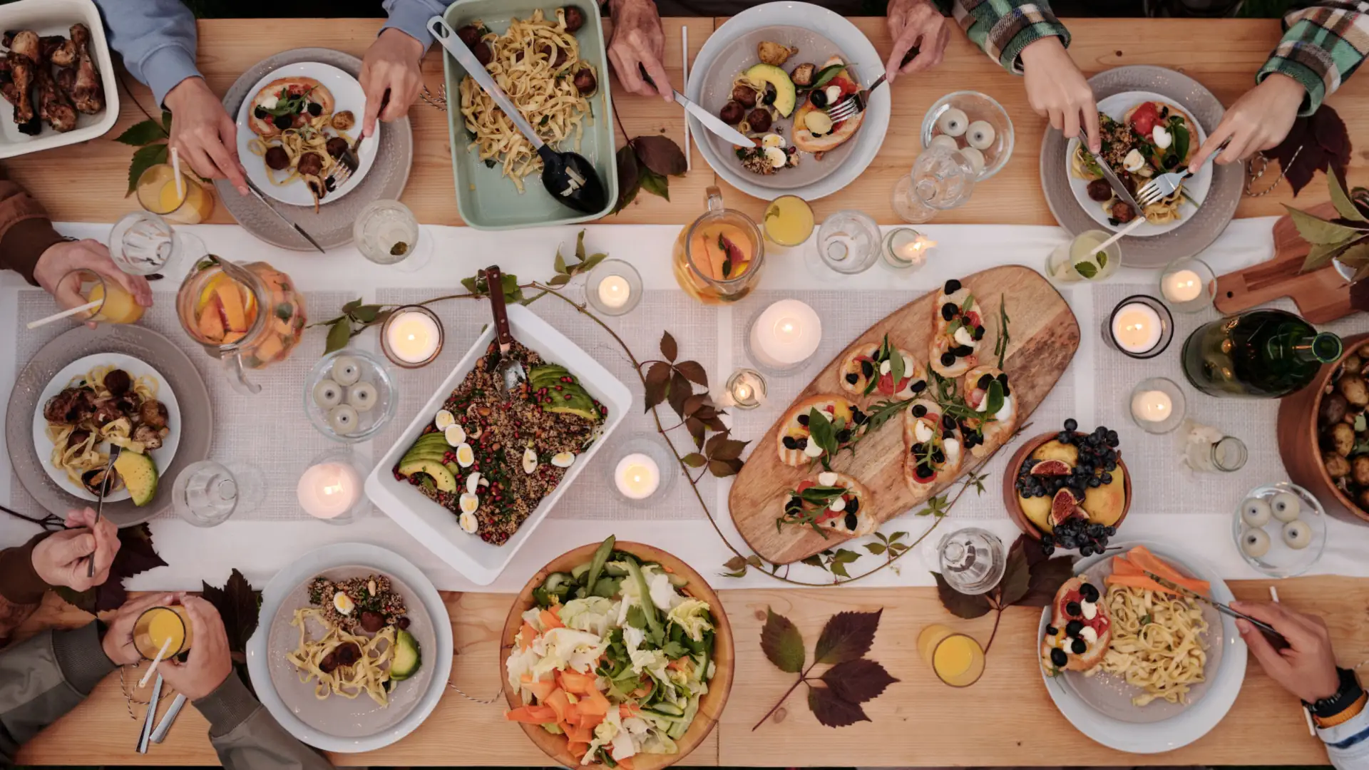 An overhead view of a long table set for a holiday meal with shared dishes, salads and candles