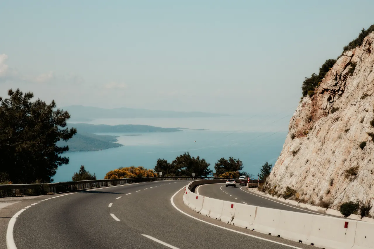 Winding road hugging a rocky cliff with stunning ocean view on a sunny day.