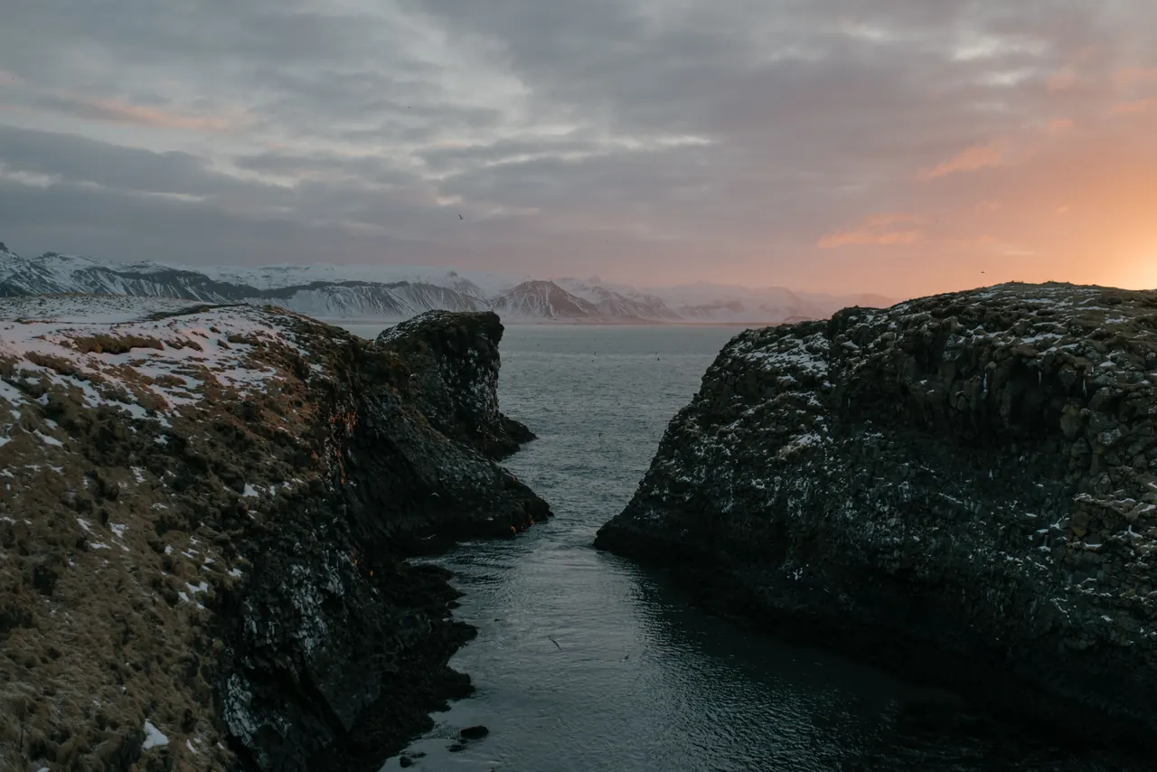 Breathtaking view of Iceland’s snowy cliffs overlooking the ocean during sunset.