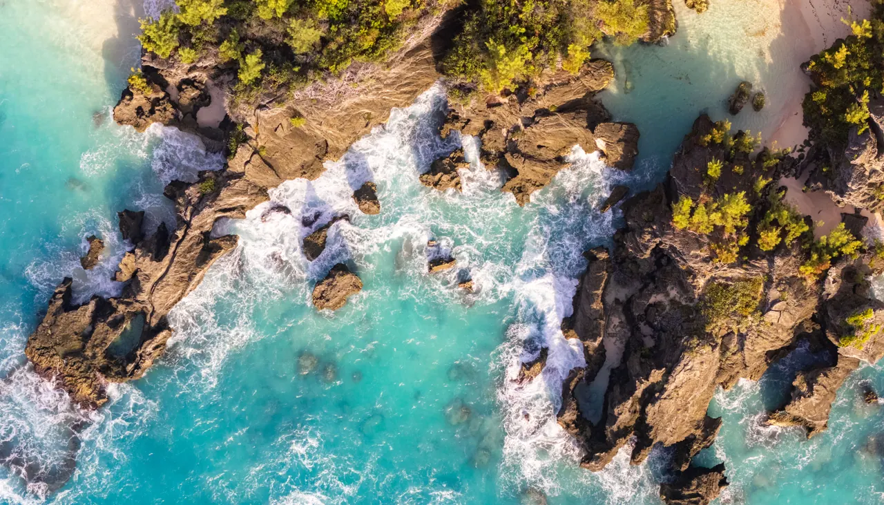 A stunning aerial view of Bermuda’s rocky coastline with turquoise waters and waves crashing.
