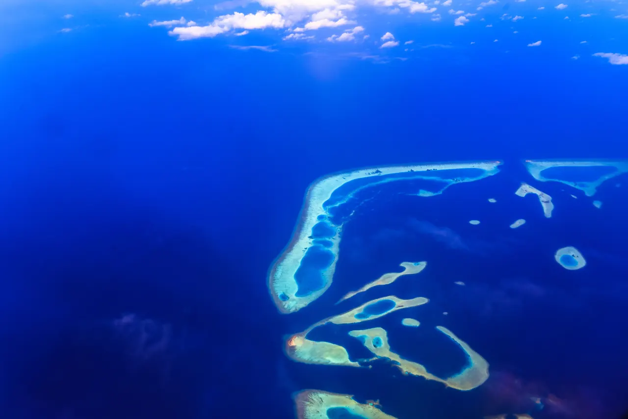 Stunning aerial photograph of vibrant coral reefs and atolls in a clear blue tropical ocean.